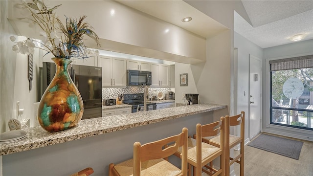 kitchen with kitchen peninsula, tasteful backsplash, light hardwood / wood-style flooring, black appliances, and light stone counters