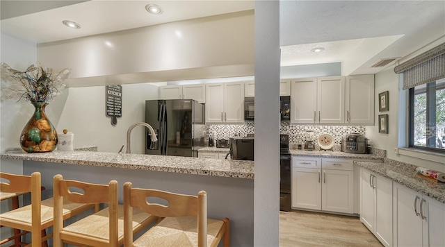 kitchen with light stone countertops, black appliances, kitchen peninsula, and white cabinets