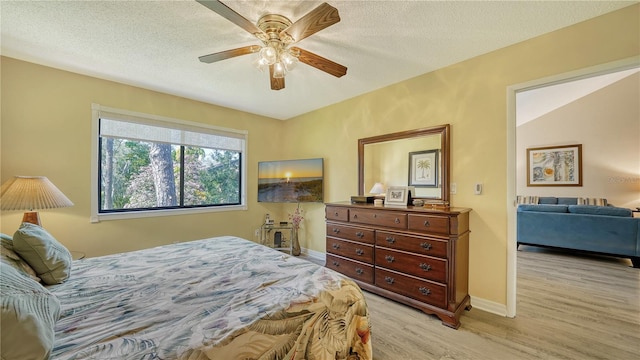 bedroom with lofted ceiling, a textured ceiling, light wood-type flooring, and ceiling fan