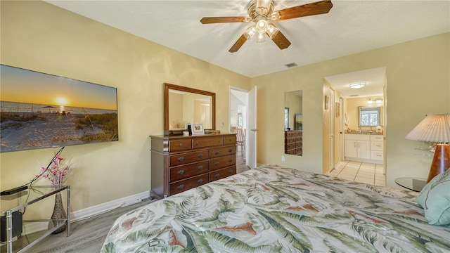 bedroom with a textured ceiling, ensuite bathroom, light wood-type flooring, and ceiling fan