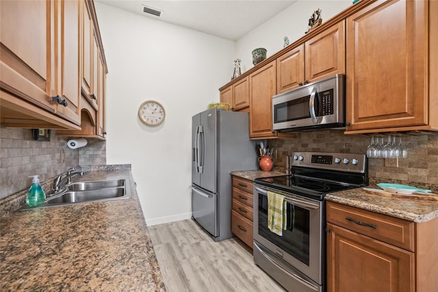 kitchen featuring appliances with stainless steel finishes, stone countertops, decorative backsplash, sink, and light hardwood / wood-style floors