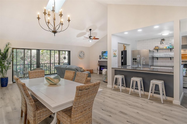 dining space with sink, light hardwood / wood-style flooring, high vaulted ceiling, and ceiling fan with notable chandelier