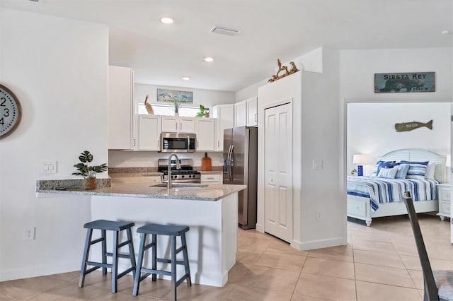 kitchen with light stone counters, white cabinetry, appliances with stainless steel finishes, a kitchen breakfast bar, and kitchen peninsula