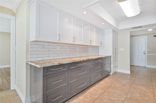 kitchen featuring backsplash, crown molding, light tile patterned floors, light stone counters, and white cabinetry