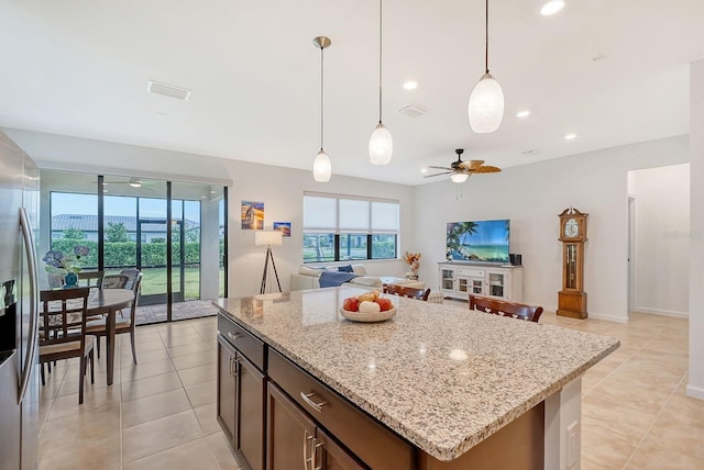 kitchen with a center island, stainless steel refrigerator with ice dispenser, ceiling fan, light stone countertops, and decorative light fixtures