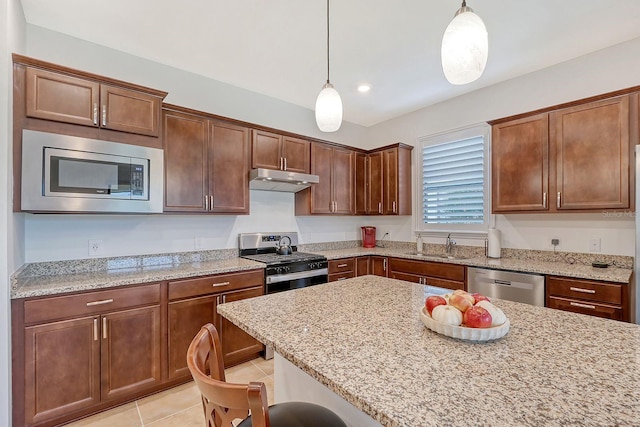 kitchen with a breakfast bar, hanging light fixtures, light tile patterned floors, appliances with stainless steel finishes, and light stone counters