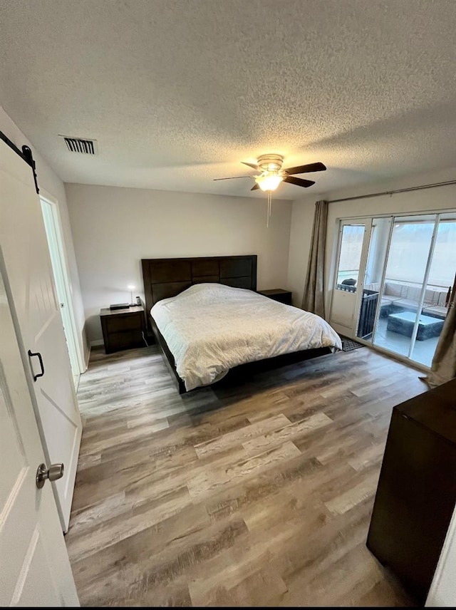 bedroom featuring access to outside, light hardwood / wood-style flooring, ceiling fan, a barn door, and a textured ceiling