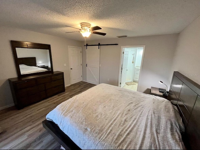 bedroom featuring connected bathroom, ceiling fan, a barn door, dark hardwood / wood-style flooring, and a textured ceiling