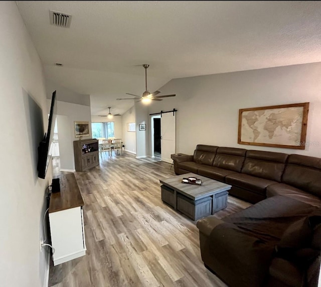 living room featuring a barn door, ceiling fan, light hardwood / wood-style floors, and vaulted ceiling