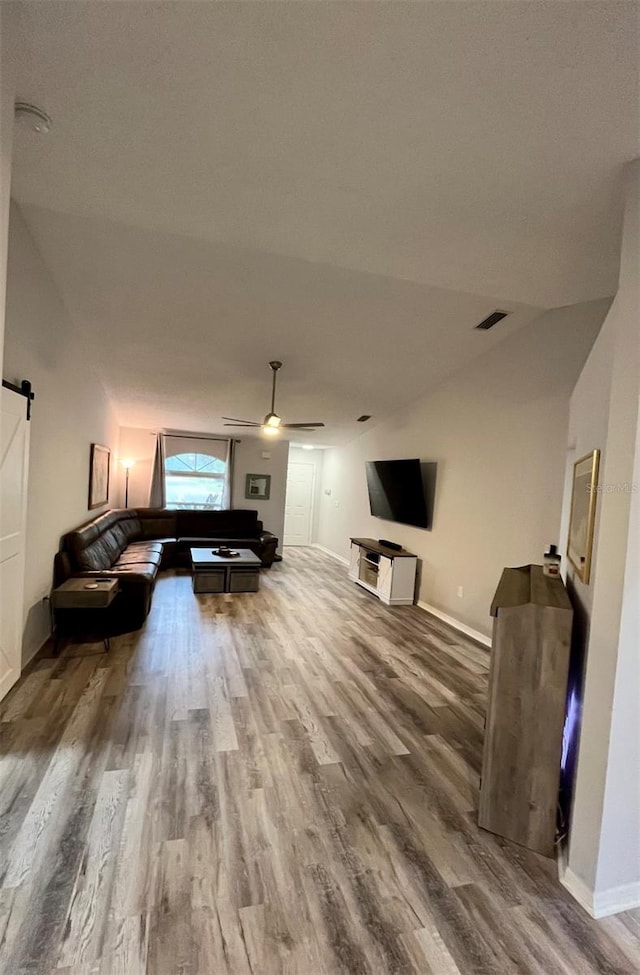 living room with a barn door, ceiling fan, wood-type flooring, and vaulted ceiling