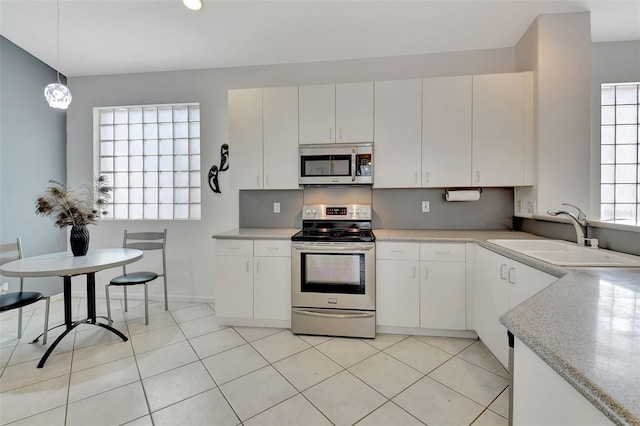 kitchen with stainless steel appliances, white cabinetry, sink, and decorative light fixtures