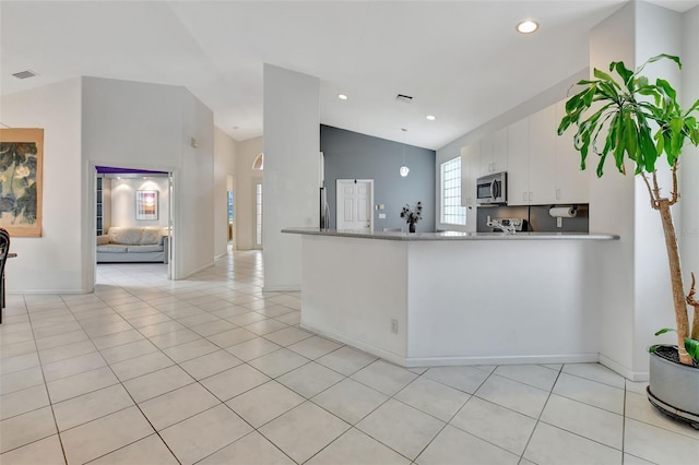 kitchen with kitchen peninsula, appliances with stainless steel finishes, light tile patterned floors, lofted ceiling, and white cabinets