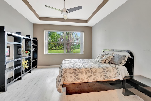 bedroom with a tray ceiling, light hardwood / wood-style floors, and ceiling fan