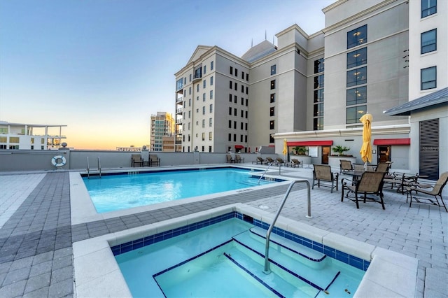 pool at dusk featuring a community hot tub and a patio