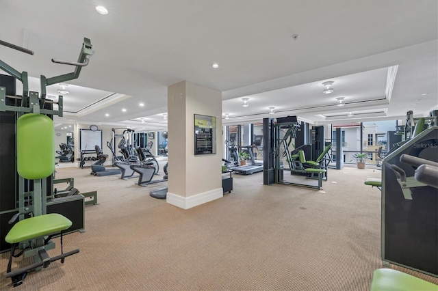 gym with a tray ceiling and light colored carpet