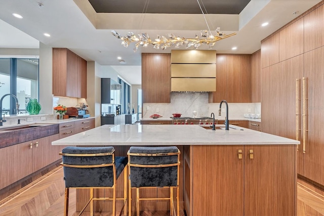 kitchen with a kitchen bar, light parquet floors, light stone countertops, and an island with sink