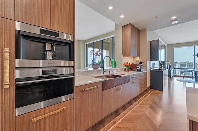 kitchen with double oven, light stone countertops, sink, and light parquet flooring