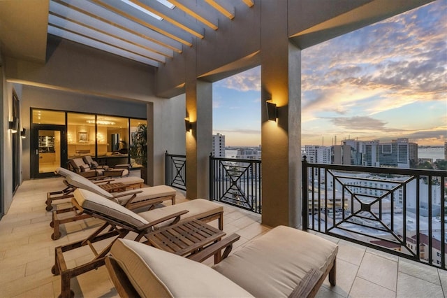 patio terrace at dusk featuring a pergola and a balcony