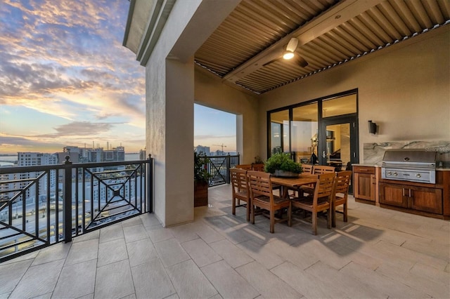 balcony at dusk featuring area for grilling, exterior kitchen, and a patio