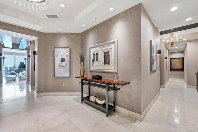 hallway featuring a tray ceiling and an inviting chandelier