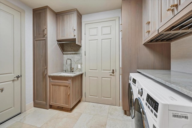 clothes washing area with washer and clothes dryer, cabinets, and sink