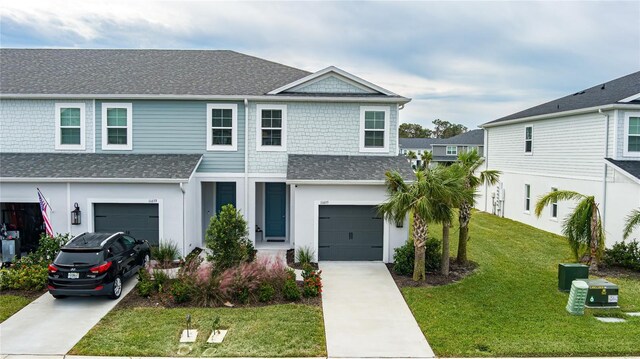 view of front facade featuring an attached garage, driveway, a shingled roof, and a front yard