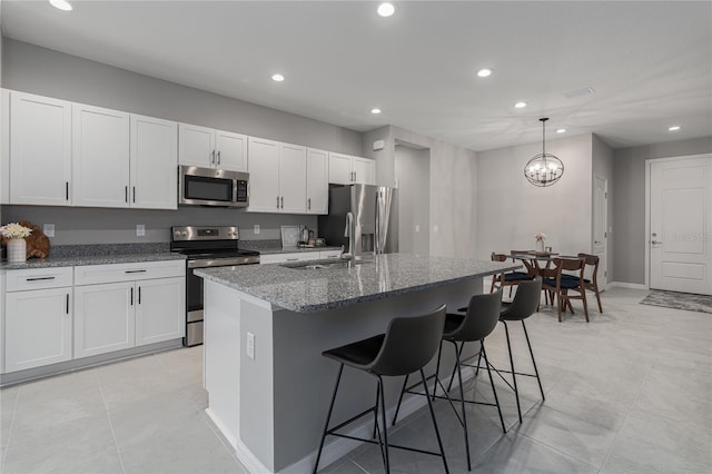 kitchen featuring white cabinetry, stainless steel appliances, light stone countertops, and a center island with sink