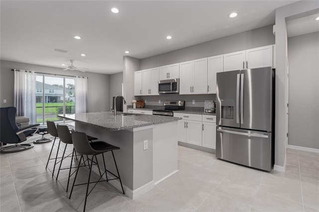 kitchen with an island with sink, sink, white cabinets, appliances with stainless steel finishes, and light stone counters