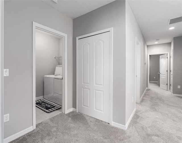 corridor featuring light carpet, a textured ceiling, and separate washer and dryer