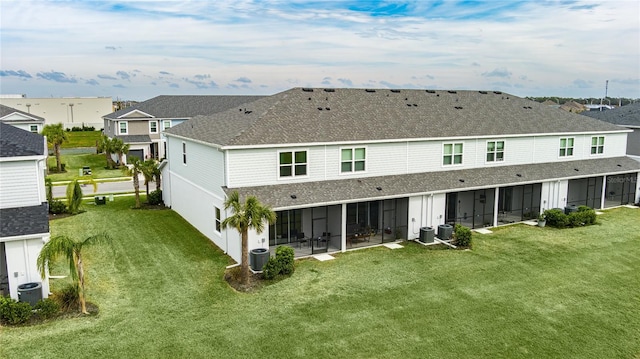 back of property with central air condition unit, a sunroom, and a lawn