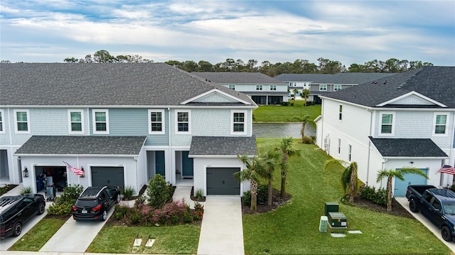 traditional-style home featuring driveway, a front yard, a residential view, an attached garage, and a shingled roof