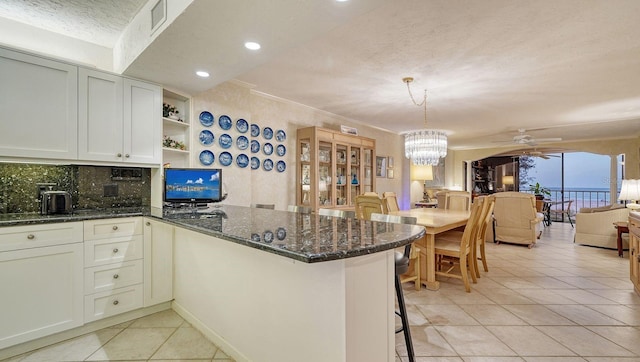 kitchen featuring kitchen peninsula, decorative backsplash, dark stone counters, a textured ceiling, and white cabinets