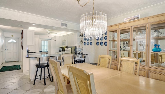 tiled dining room featuring ornamental molding, a textured ceiling, a notable chandelier, and sink