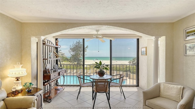 tiled dining area with a water view, a wealth of natural light, ceiling fan, and ornamental molding