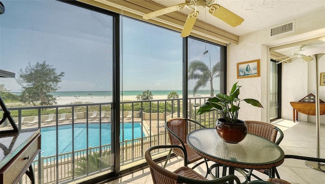 sunroom with ceiling fan, a water view, and a beach view