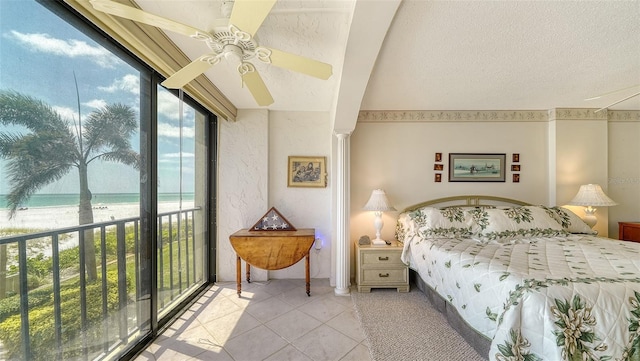 tiled bedroom featuring a water view, a view of the beach, ceiling fan, access to exterior, and a textured ceiling