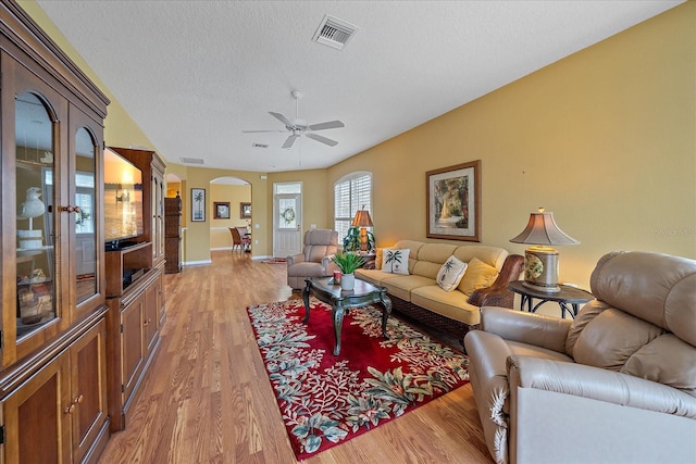 living room with a textured ceiling, light wood-type flooring, and ceiling fan