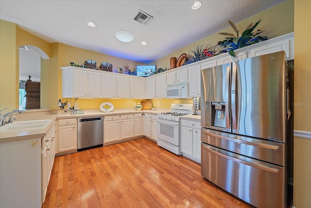 kitchen with a textured ceiling, white cabinets, stainless steel appliances, and light wood-type flooring