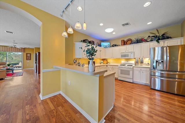 kitchen featuring white appliances, a textured ceiling, kitchen peninsula, hanging light fixtures, and white cabinetry