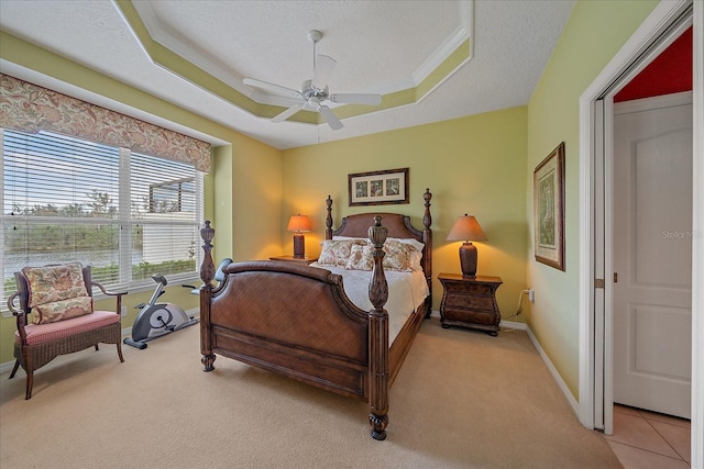 bedroom featuring a textured ceiling, light colored carpet, a tray ceiling, and ceiling fan