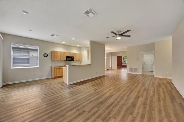 unfurnished living room featuring ceiling fan, a textured ceiling, sink, and light wood-type flooring