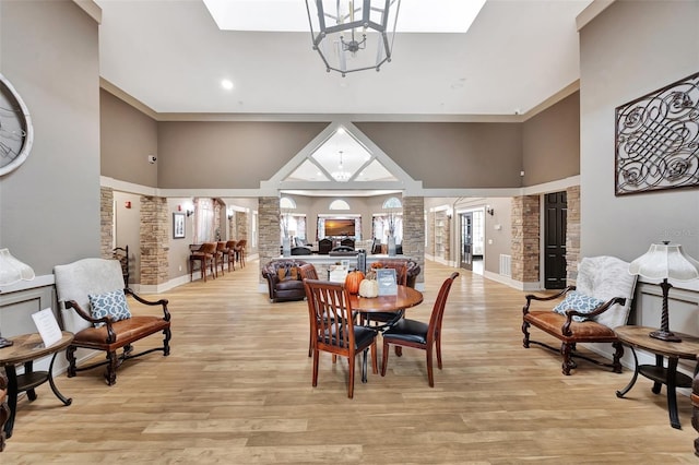 dining area with a high ceiling, an inviting chandelier, crown molding, ornate columns, and light wood-type flooring