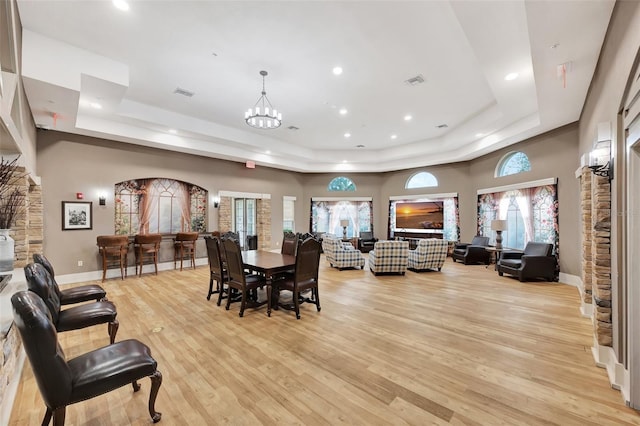 dining space with light hardwood / wood-style floors, plenty of natural light, and a raised ceiling