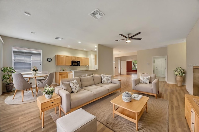 living room with light hardwood / wood-style floors, ceiling fan, and sink