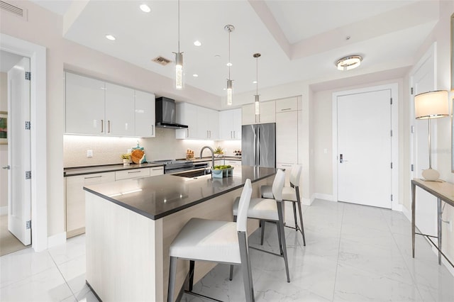 kitchen with wall chimney range hood, stainless steel fridge, dark countertops, a sink, and light marble finish flooring