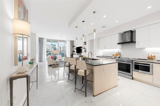 kitchen with white cabinets, a kitchen breakfast bar, a kitchen island with sink, stainless steel appliances, and wall chimney exhaust hood