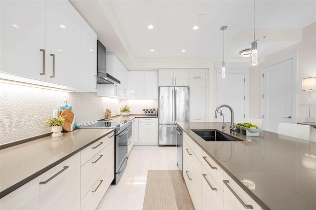 kitchen with wall chimney range hood, sink, appliances with stainless steel finishes, hanging light fixtures, and white cabinets