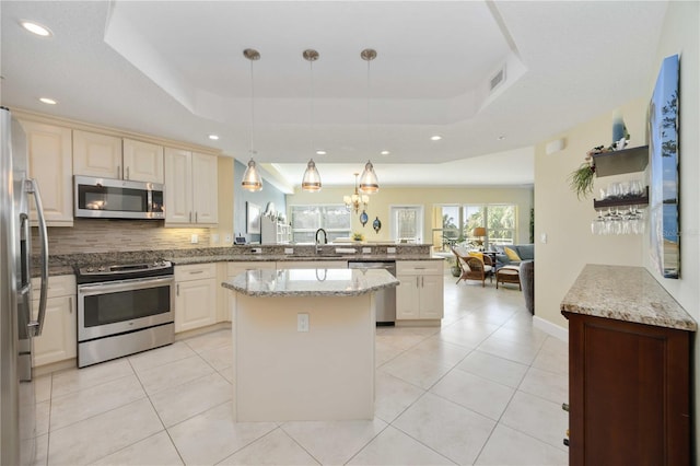 kitchen with a raised ceiling, appliances with stainless steel finishes, hanging light fixtures, and kitchen peninsula