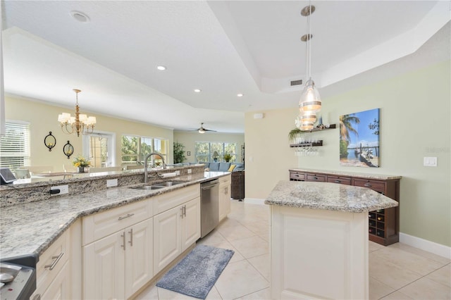 kitchen featuring sink, stainless steel dishwasher, a tray ceiling, a kitchen island, and pendant lighting