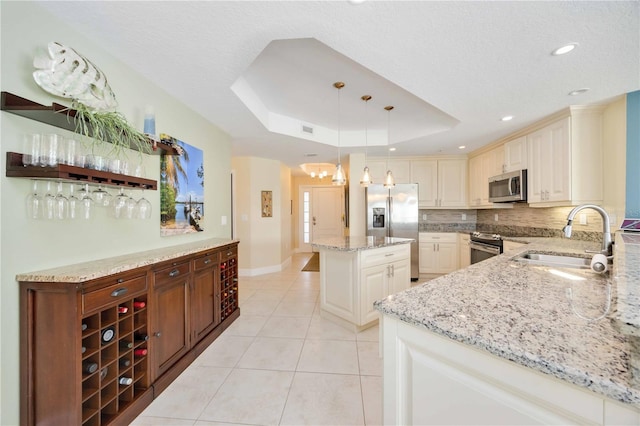 kitchen featuring sink, hanging light fixtures, light stone counters, a tray ceiling, and stainless steel appliances